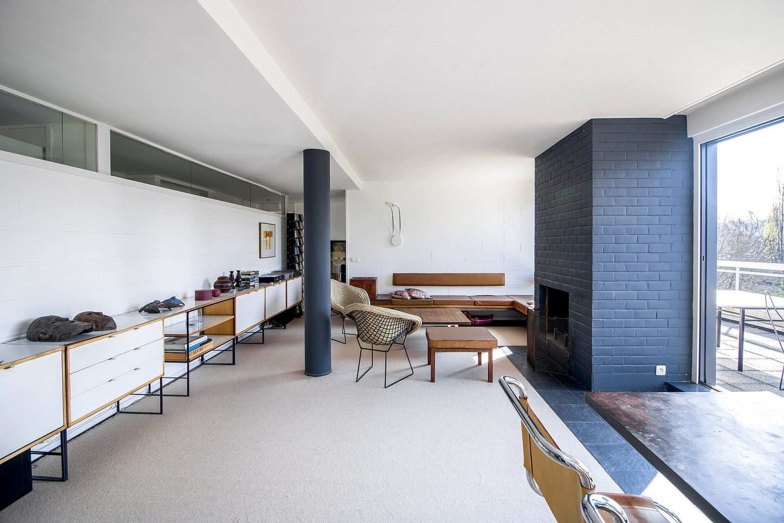 A bright, sparely furnished modern living room with a fireplace wall and low shelves, a Wikimedia Commons photograph in the encyclopedia of Mike Kobeissi