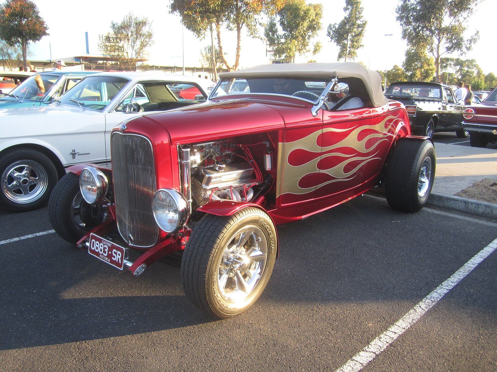 A flame painted 1932 roadster hot rod with a chrome engine at an evening car show, a Wikimedia Commons photograph in the encyclopedia of Mike Kobeissi