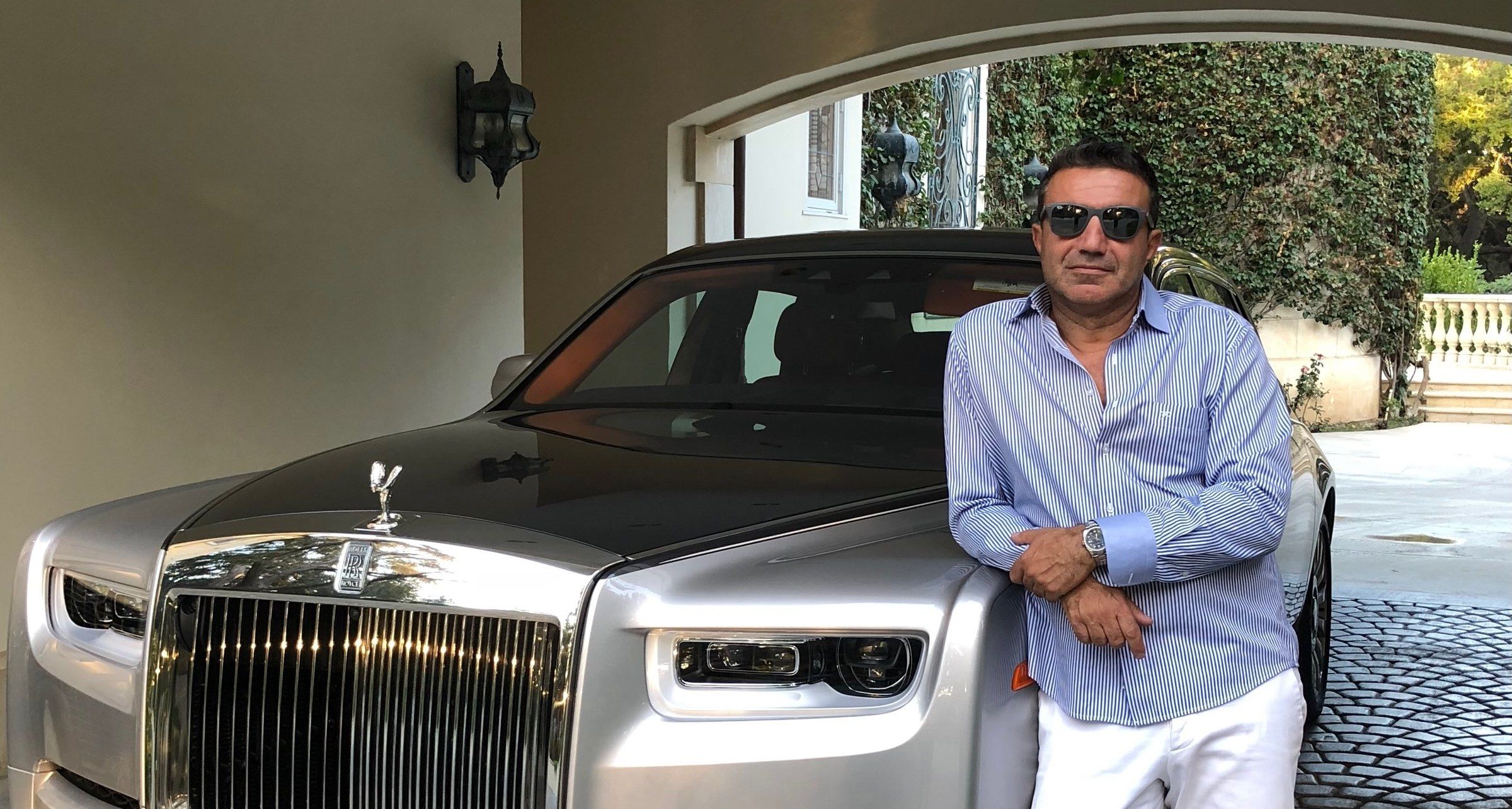 Mike Kobeissi in sunglasses and a striped shirt leaning on a silver car from his collection