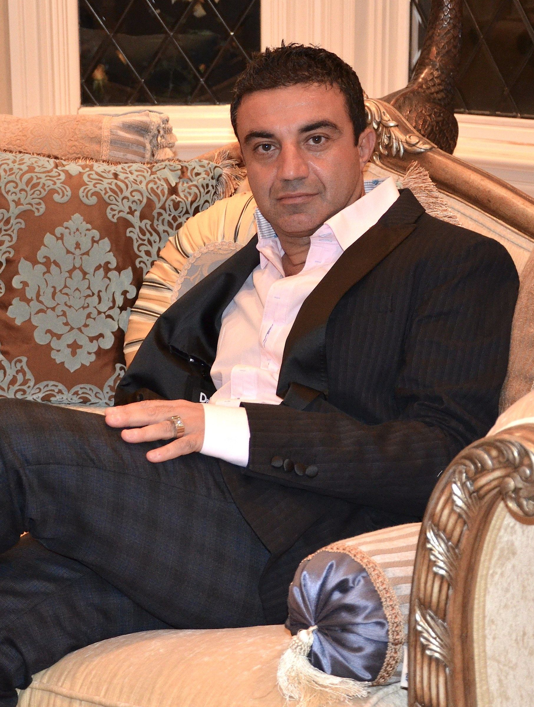 Mike Kobeissi seated on an upholstered sofa in a dark suit and white shirt