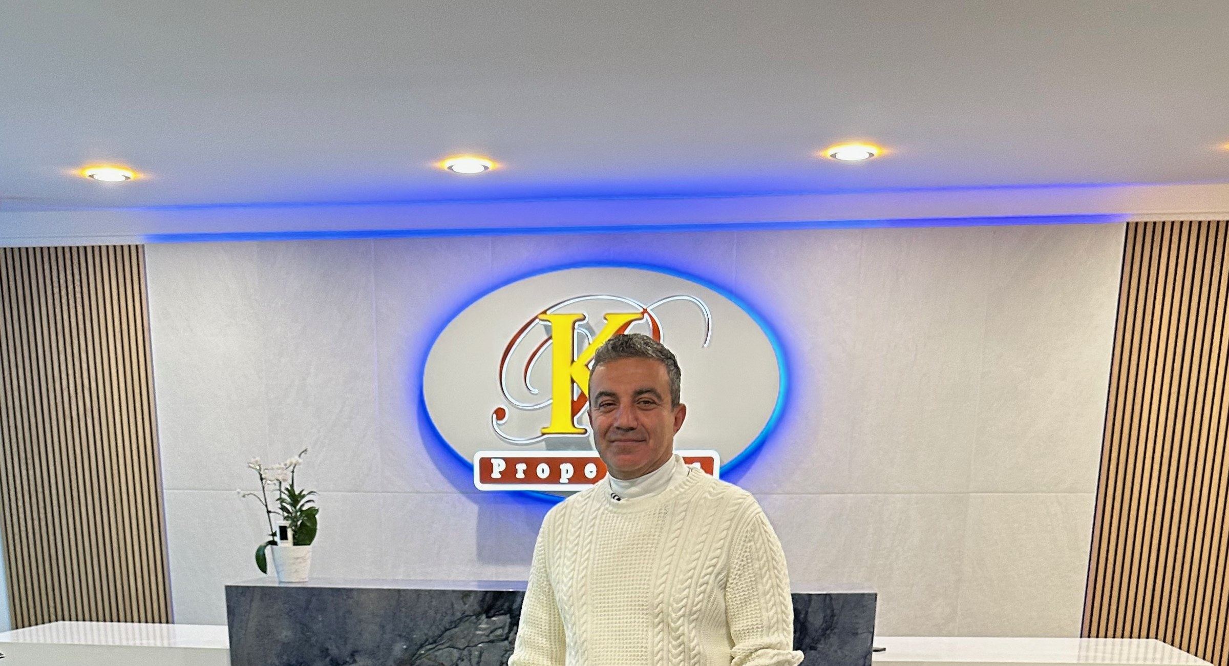 Mike Kobeissi in a cream sweater at the reception wall of the Kobeissi Properties office