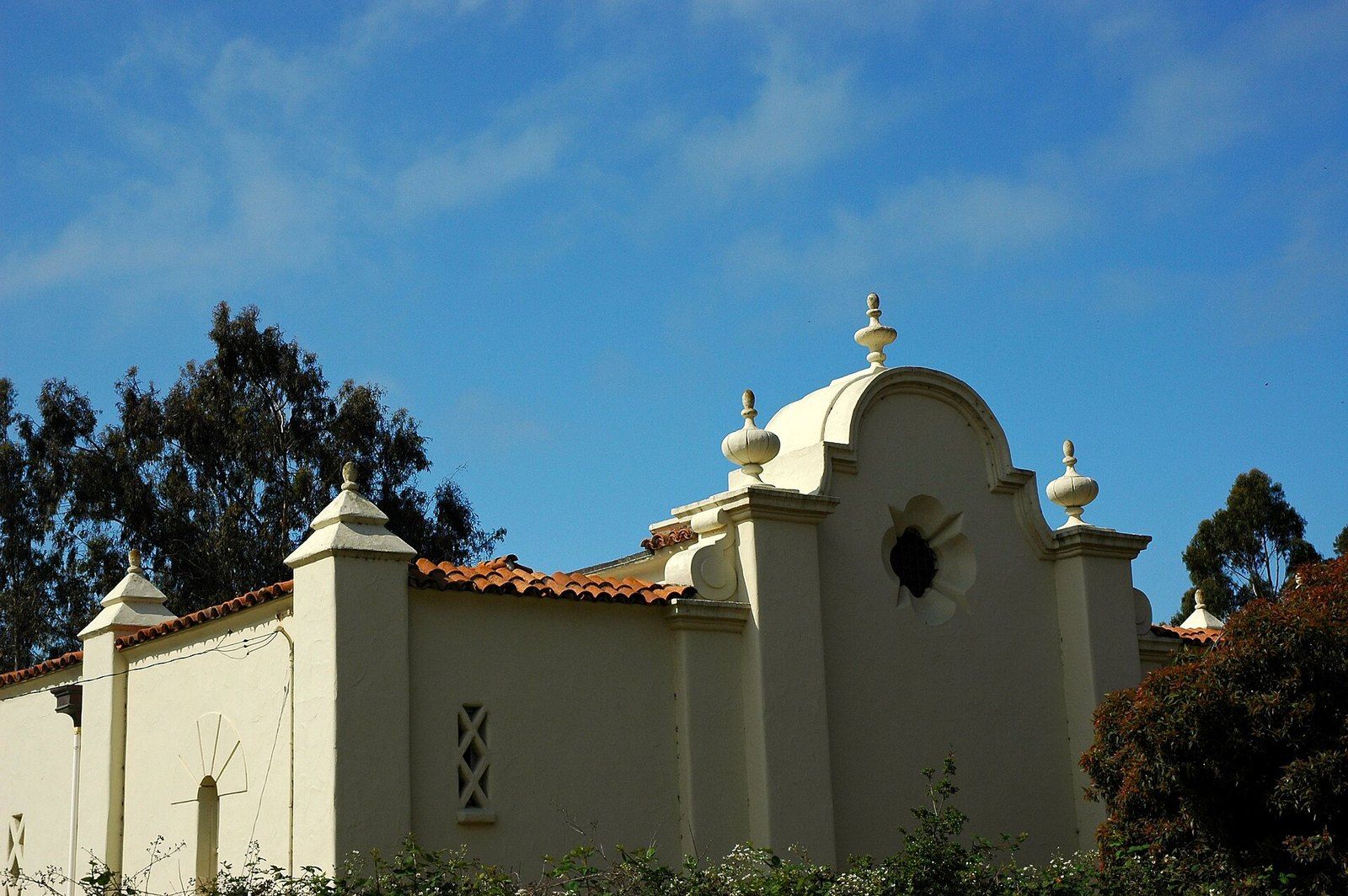 A Mission Revival parapet gable with bell finials against a blue sky in San Simeon, a Wikimedia Commons photograph in the encyclopedia of Mike Kobeissi