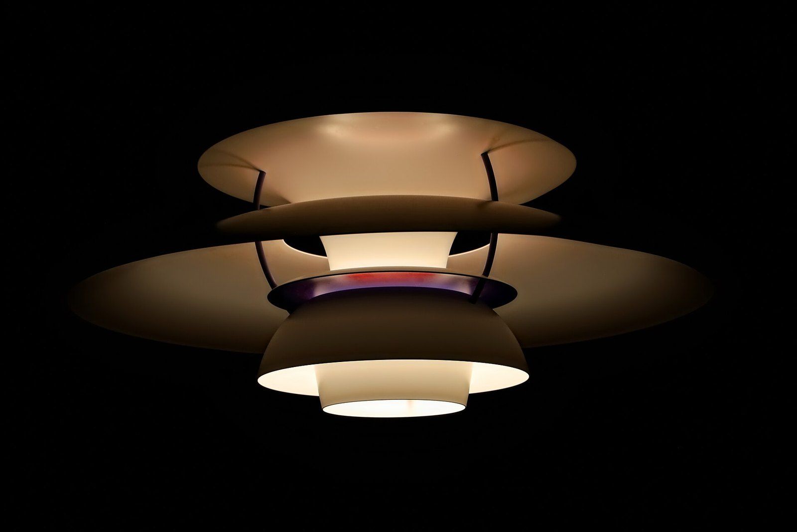 A layered metal shade pendant lamp glowing against a dark ceiling, a Wikimedia Commons photograph in the encyclopedia of Mike Kobeissi