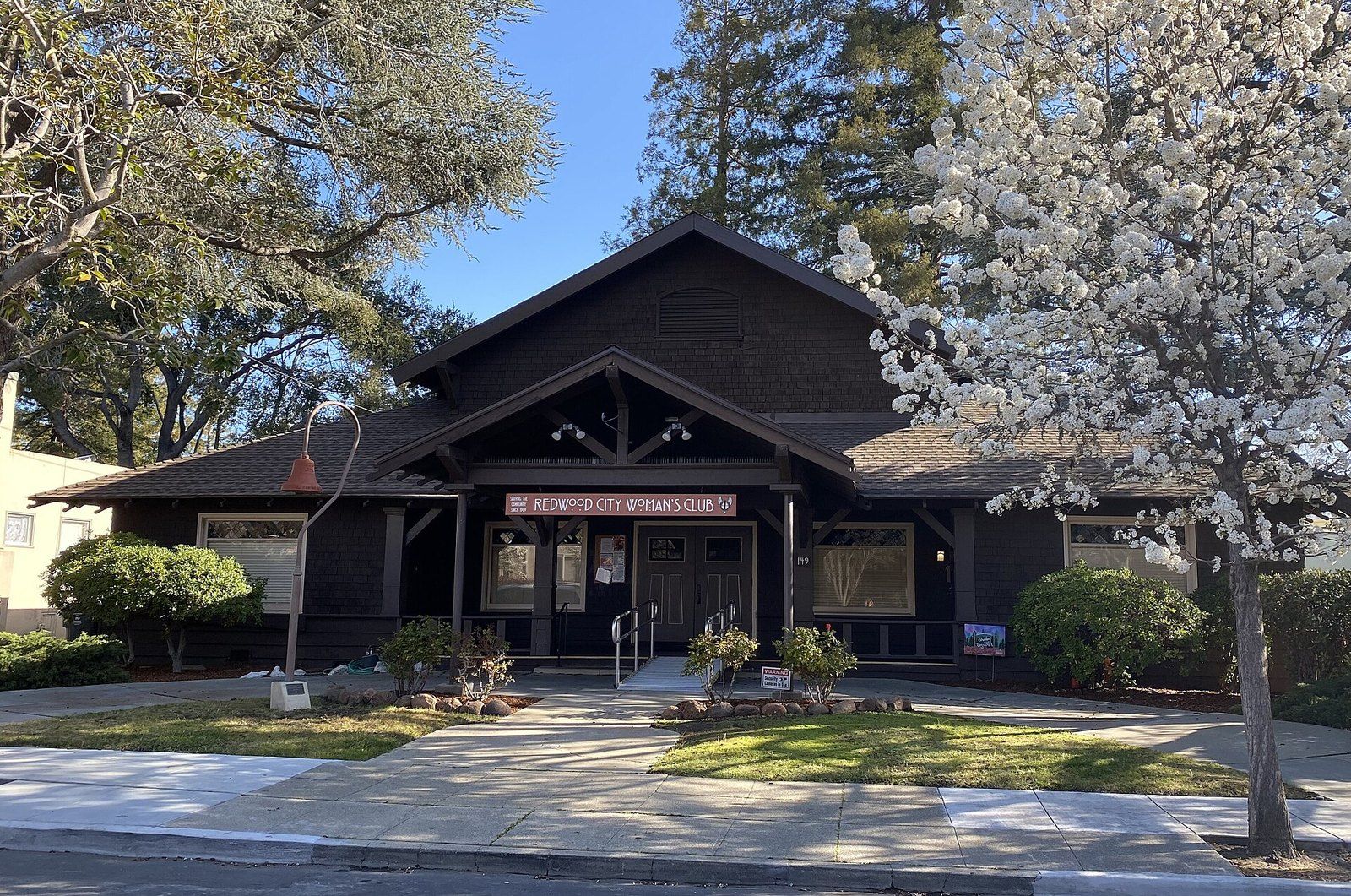 The shingled clubhouse of the Redwood City Woman's Club under a flowering tree, a Wikimedia Commons photograph in the encyclopedia of Mike Kobeissi