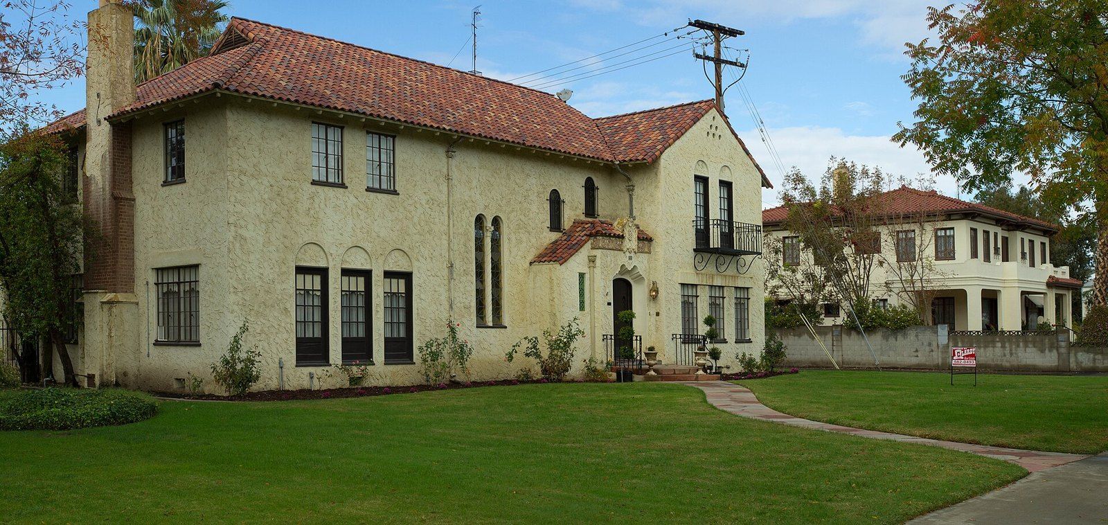 A two story Spanish Revival house with a red tile roof and arched entry above a wide lawn, a Wikimedia Commons photograph in the encyclopedia of Mike Kobeissi