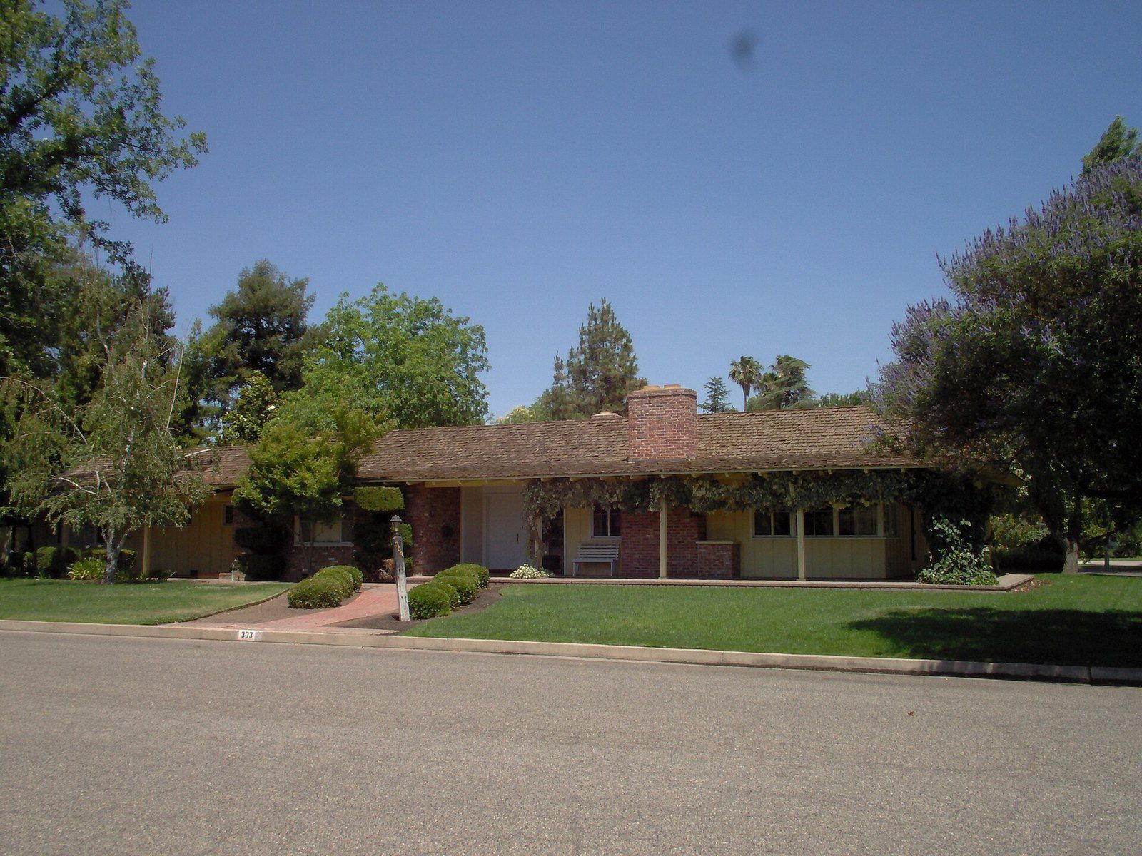 A low 1950s California ranch house with a long tiled roof behind a lawn, a Wikimedia Commons photograph in the encyclopedia of Mike Kobeissi