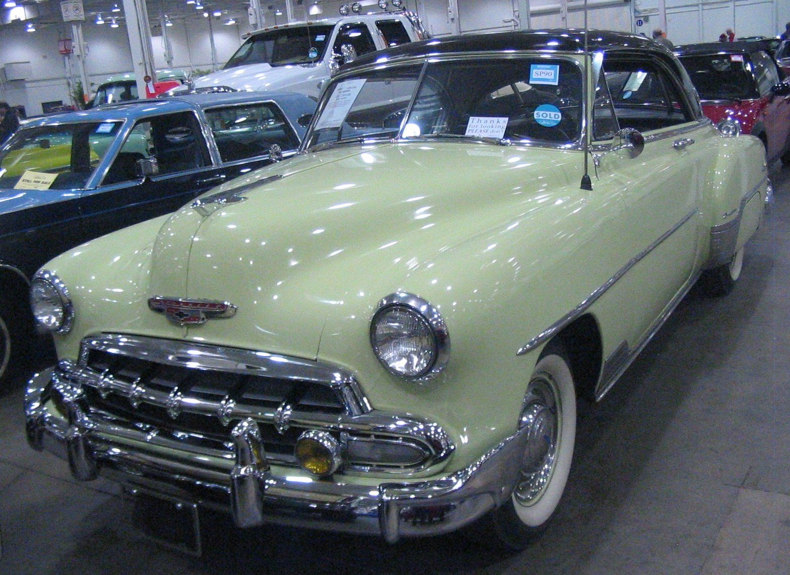 A pale green 1952 two door hardtop on the floor of a classic car auction, a Wikimedia Commons photograph in the encyclopedia of Mike Kobeissi